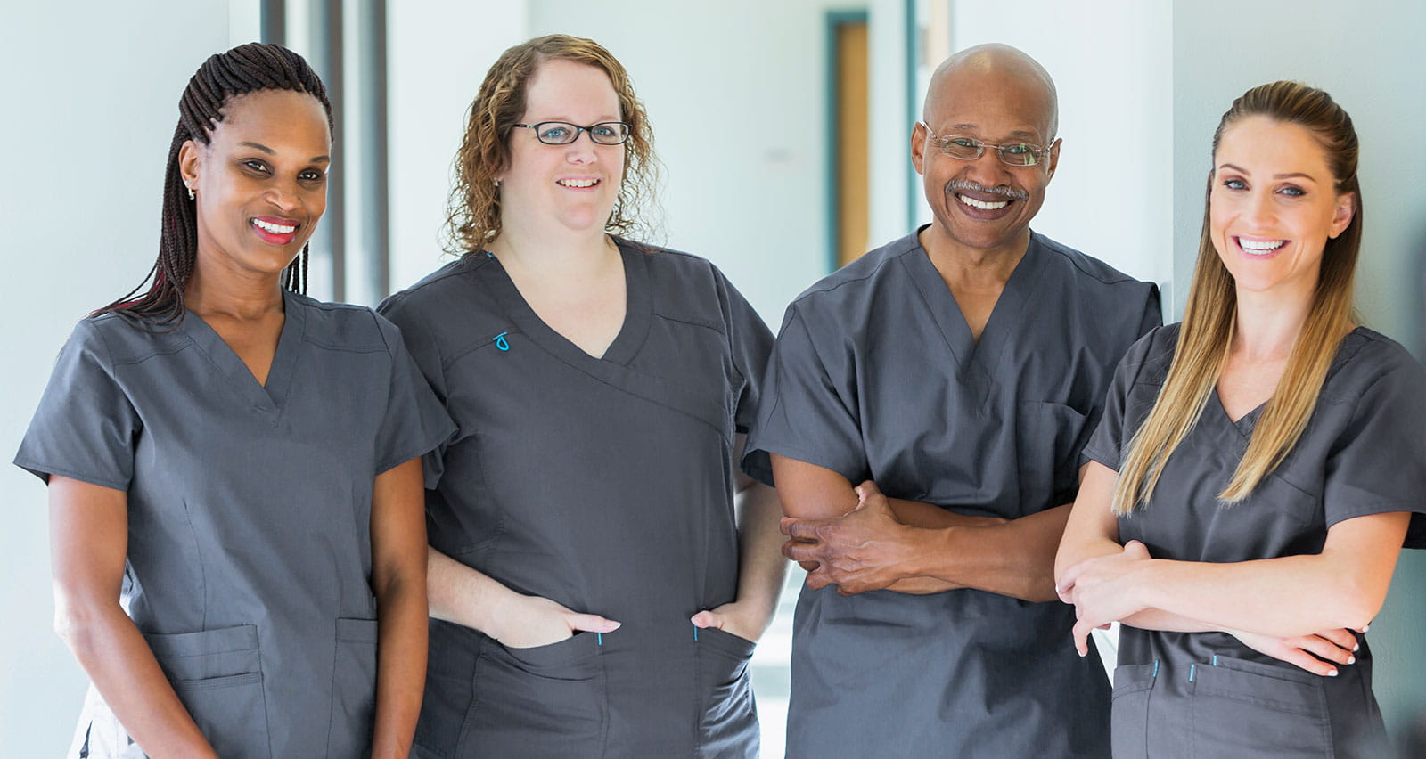 A team of four multi-ethnic medical professionals standing in a corridor, wearing scrubs