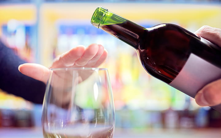 A woman’s hand rejecting more alcohol from a wine bottle in a bar