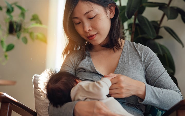 A young mother breastfeeding her baby daughter while sitting on sofa at home