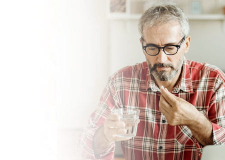 A middle aged man taking aspirin with a glass of water in front of laptop