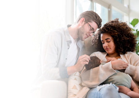 A young woman breastfeeds her infant son as her husband smiles at the baby