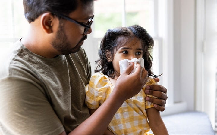A father wiping his toddler daughter's nose