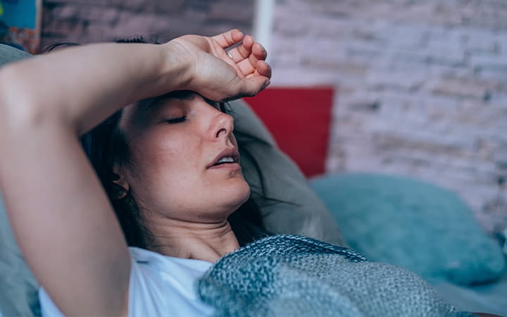 A woman suffering from a headache is lying in bed