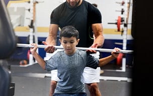 Coach assists young boy lifting weights