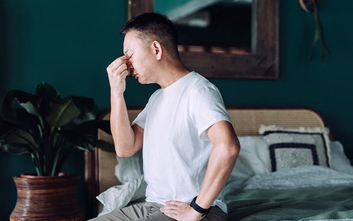 Man with headache sits on bed