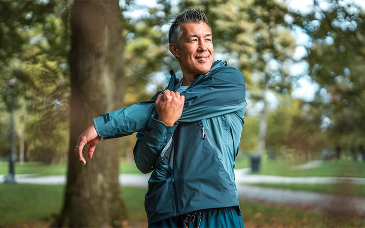 An middle-aged Asian man practices outdoor fitness by stretching in a public park