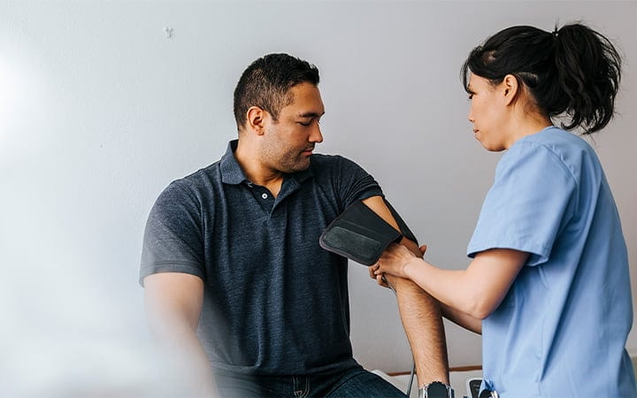 A female medical professional checking a male patient's blood pressure in an examination room 