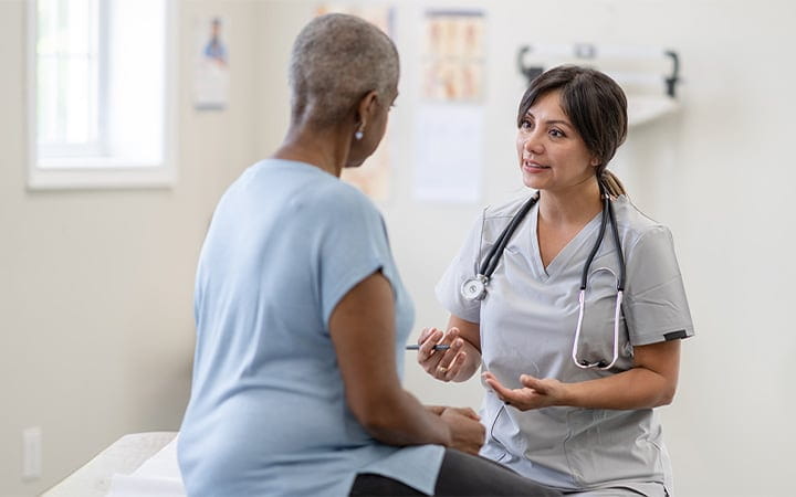 An older woman sits up on an exam table for a cancer check-up