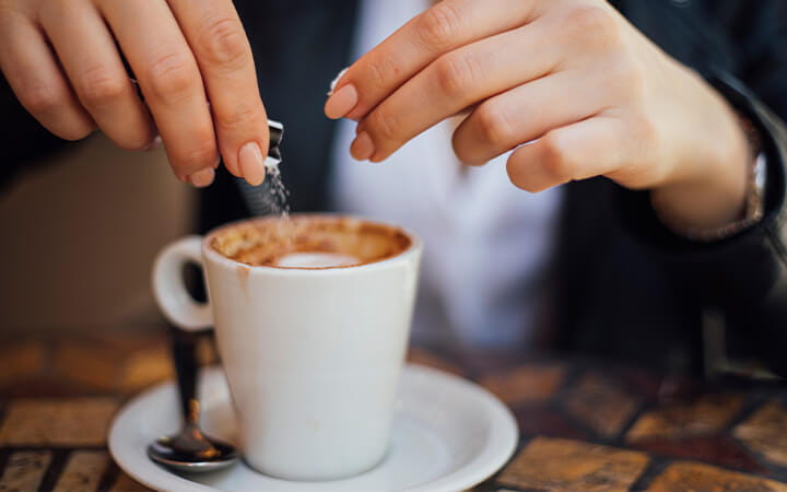 person adding sweetener to cup of coffee