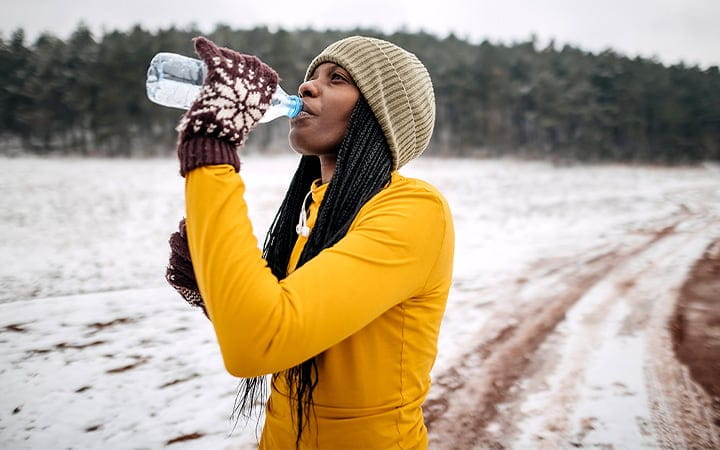 A woman drinks water after training outdoors on a snowy day