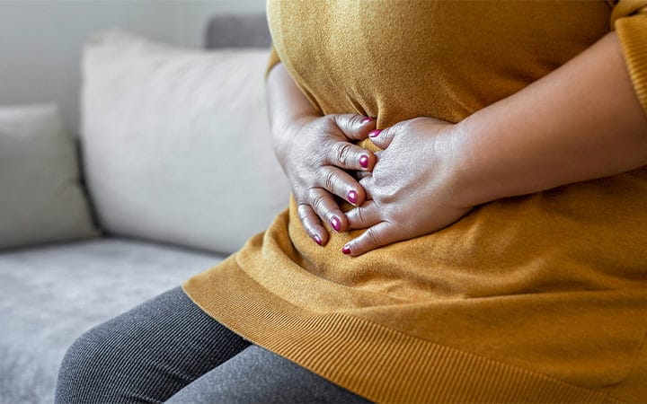 A woman in discomfort holds her midsection while seated on a couch