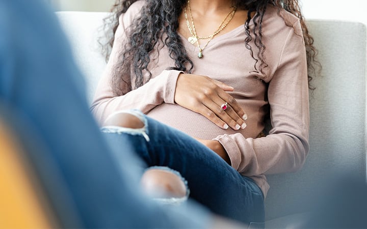 A pregnant young adult woman with her hands on her belly