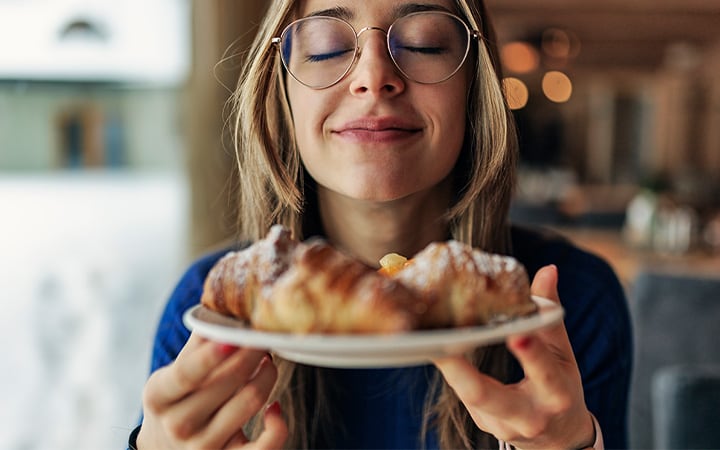 Teenage girl having breakfast in restaurant. She is smelling fresh, warm croissants