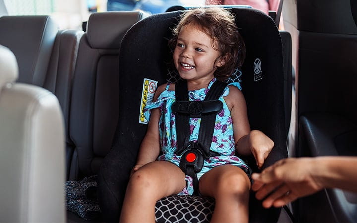 A cute three year old girl sits in her car seat and giggles with excitement