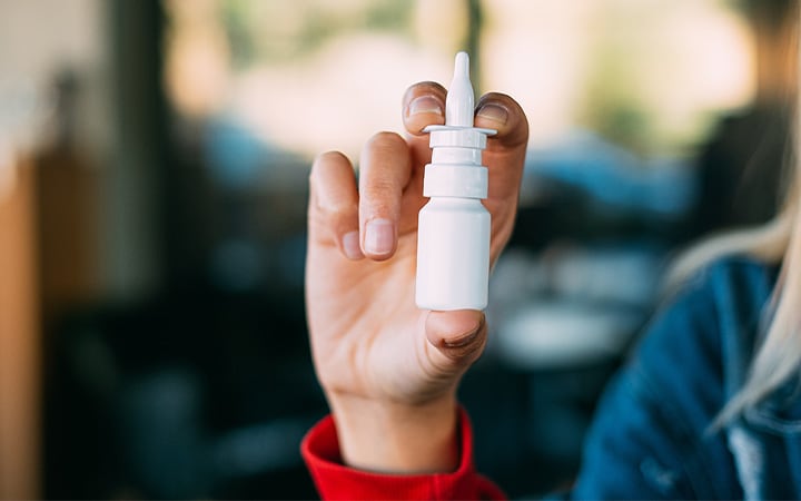 A young woman holding a bottle of nasal spray