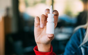 A young woman holding a bottle of nasal spray