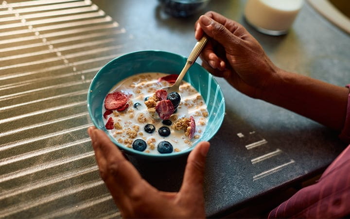 Close-up of a woman’s hands holding a bowl of muesli with milk, blueberries, and strawberries in a modern kitchen