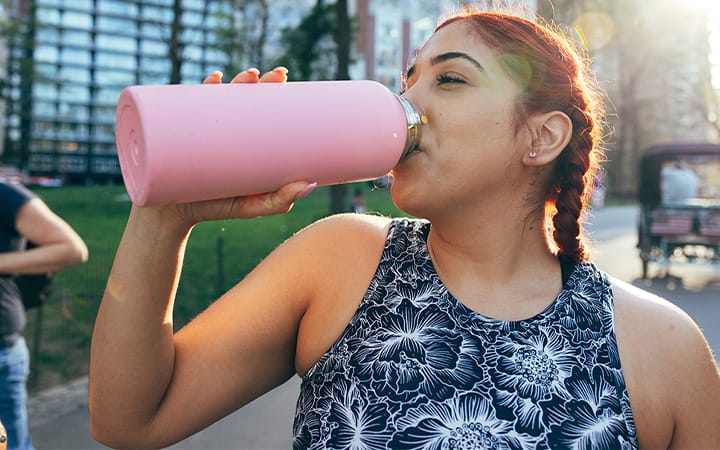 A woman drinks from a stainless steel water bottle while jogging and enjoying the morning