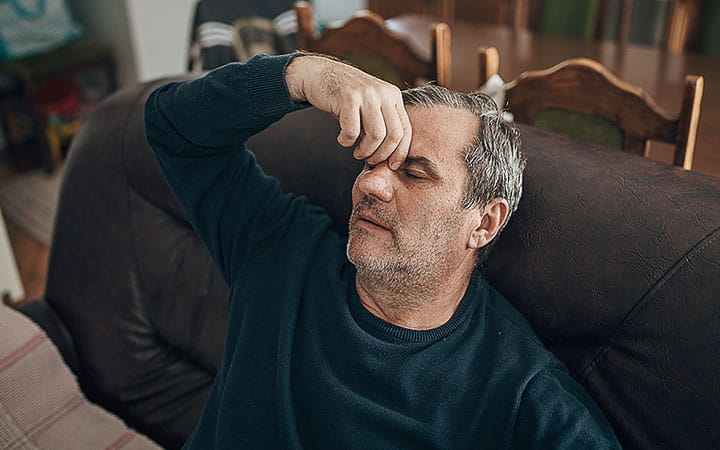 A man holds the bridge of his nose while sitting back