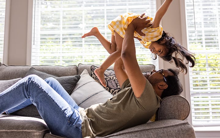 A father lifting his daughter in the air while lying on a couch