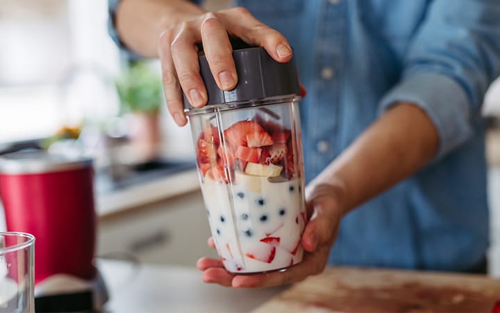 Close up of hands holding a blender containing fruits and milk for a healthy fruit smoothie