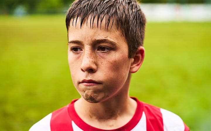 Close-up of a young boy standing in the mud on a field playing soccer