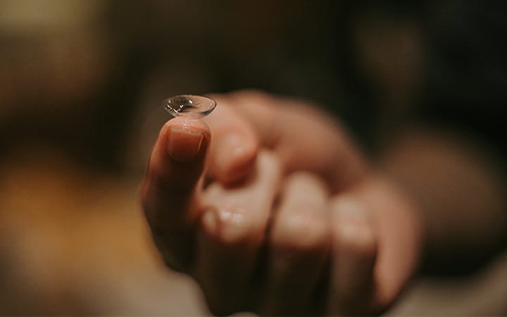 A hand holding a single contact lens