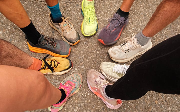 Middle-aged social running club members showing colorful sports shoes in a huddle circle