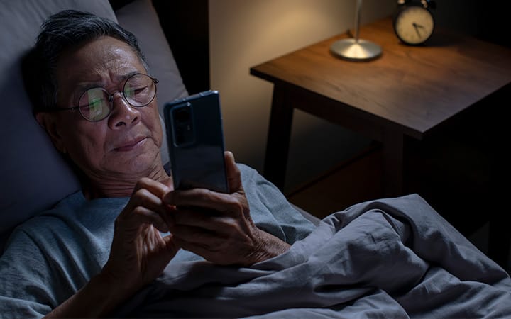 A concerned senior man scrolling on a mobile phone while in bed