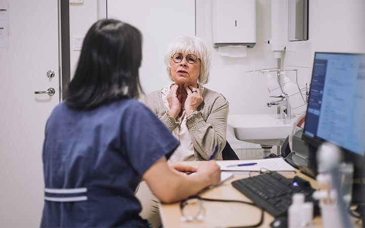 A senior woman explaining a throat problem to her otolaryngologist