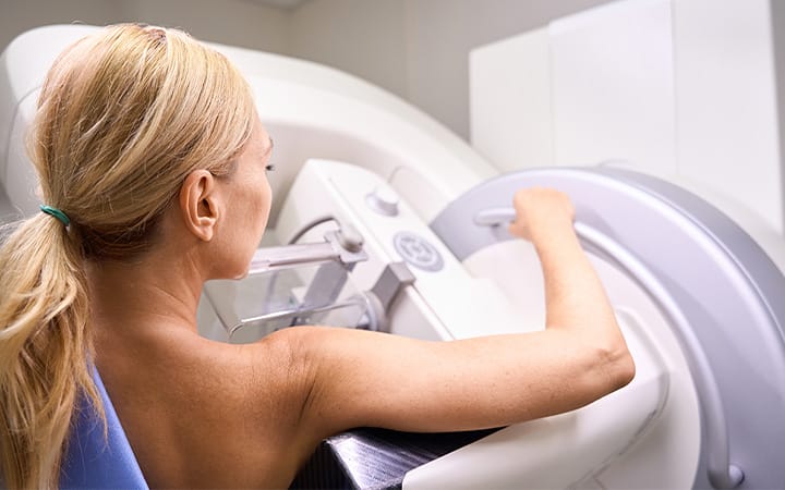 Back view of a woman undergoing digital breast tomosynthesis on modern diagnostic equipment