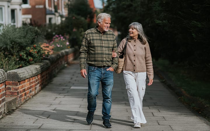 A mature man and woman stroll down a footpath beside a row of terrace houses in a beautiful residential district