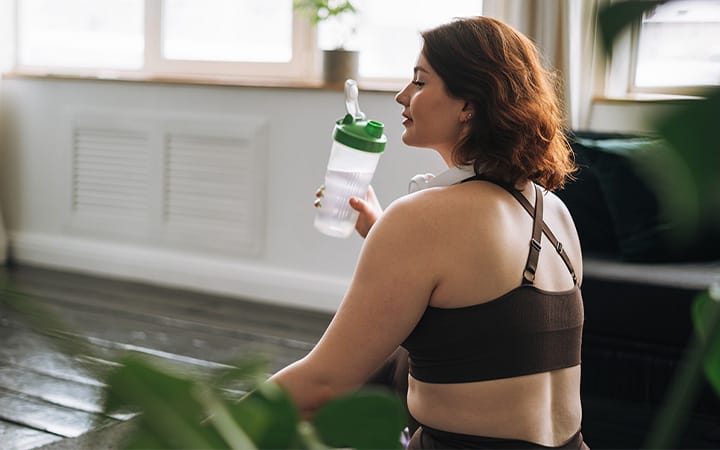 A young woman in plus-size sports clothes training and drinking water at home