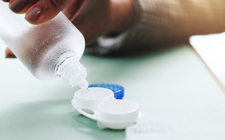 Close-up of hands pouring contact lens cleaning solution from a bottle