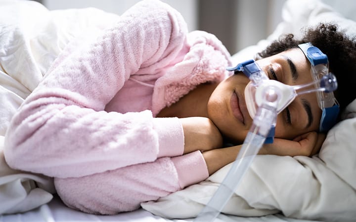 A woman in bed wearing a sleep apnea oxygen mask and CPAP device