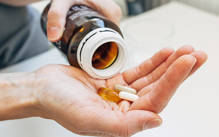 Close-up of a patient pouring large vitamin capsules from a bottle into their hand
