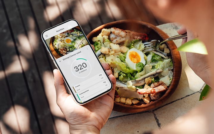 hand holding a cell phone showing a meal tracking app near a bowl of salad on a table