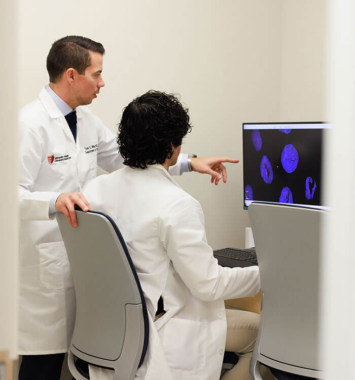Tyler Miller, MD standing in front of computer screen with another person sitting in chair looking at image of CAR T scan.