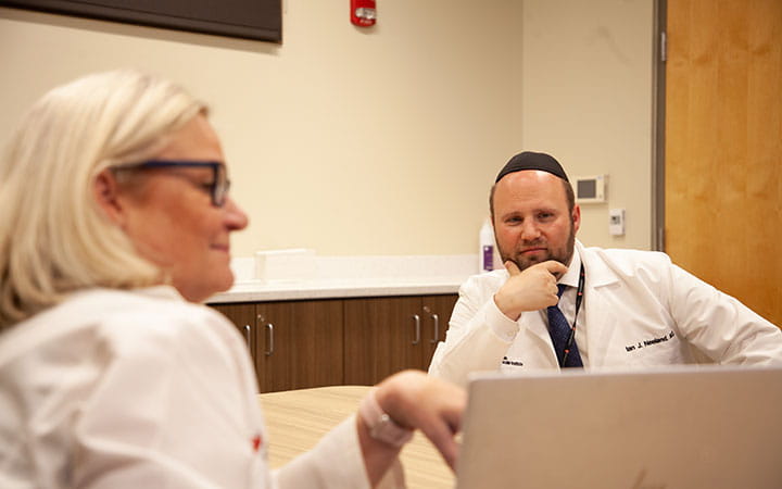 Ian Neeland, MD pictured with colleague at conference table looking at laptop computer screen in discussion.