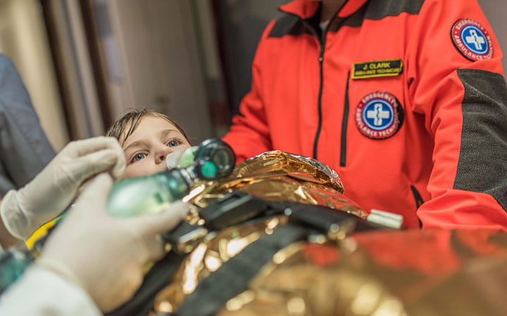 Doctors using oxygen mask on pediatric patient in hospital's corridor.