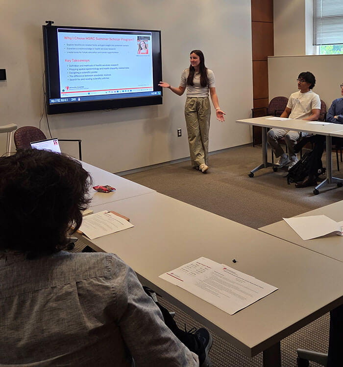 Student is presenting in front of slide screen during the Health Services Research Center Summer Scholar Program 2025.