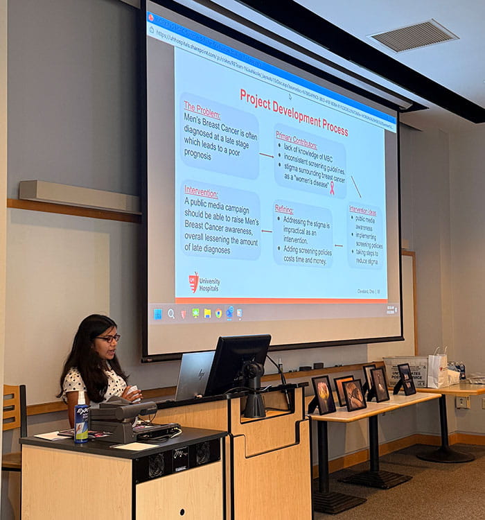 Student from the University Hospitals Health Services Research Center 2026 Summer Scholar Research Program presenting in front of power point presentation.
