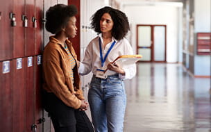 Female teacher talking to af emale teenage student in school hallway