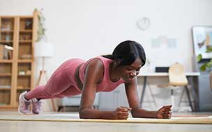 Full length portrait of young African-American woman doing plank exercise at home