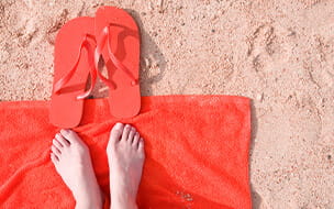 A close up of feet on an orange towel with flip flops at the beach