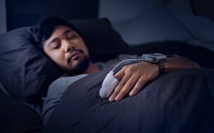 Asian man wearing a blood oxygen saturation monitor in bed for an at home sleep study test for sleep apnea.