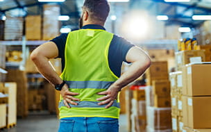 Rear view of a male warehouse worker grabbing lower back in pain