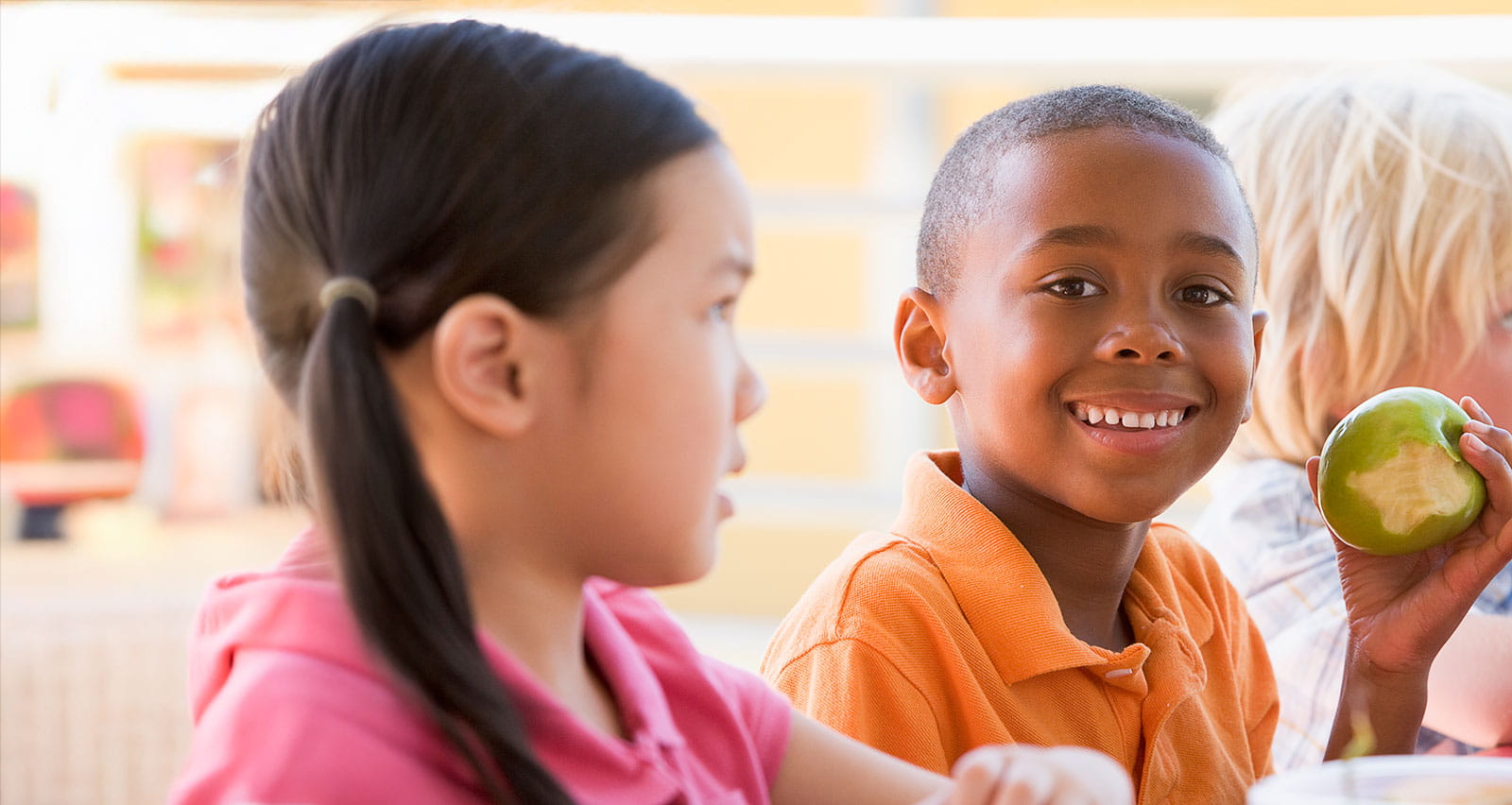 Kindergarten-age children eating lunch and smiling at camera