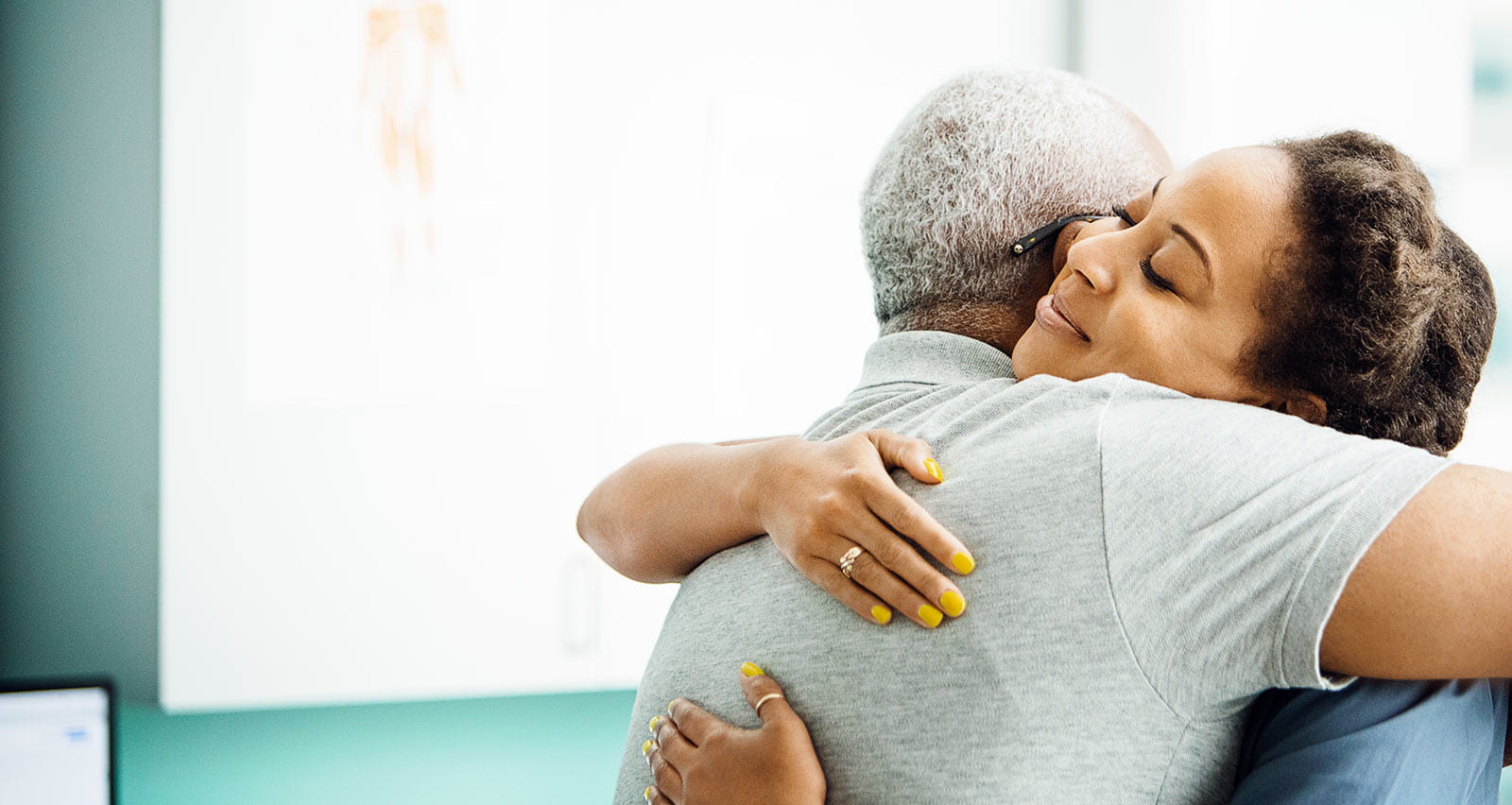 Side view of female doctor embracing senior male patient in exam room