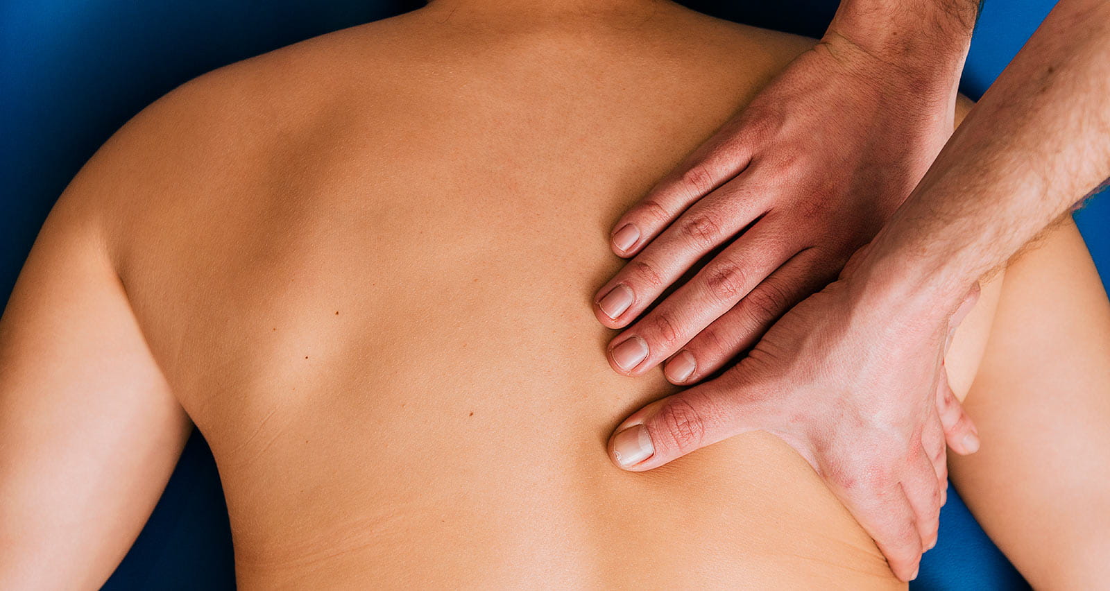 An osteopath rubbing and kneading the back of a patient during rehabilitation session in clinic